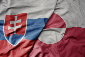 big waving national colorful flag of greenland and national flag of slovakia .