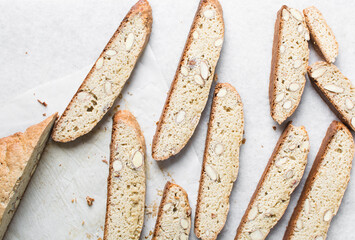 almond biscotti on white parchment lined tray, almond cantucci cookies on a white chopping board, flatlay of slices of biscotti cookies or twice baked cookies