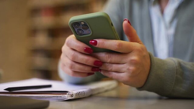 Close-up female hands using smartphone, typing online messaging in sunny room. Professor making notes in notebook, writing thesis, information, create plan or time schedule. Business education study
