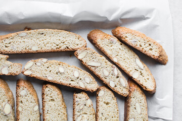 almond biscotti on white parchment lined tray, almond cantucci cookies on a white chopping board, flatlay of slices of biscotti cookies or twice baked cookies