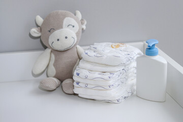 A stack of diapers, plush animal and baby supplies on changing table