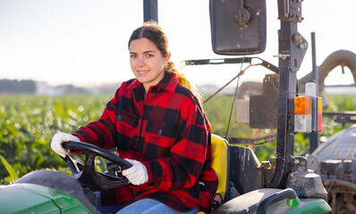 Young smiling female farmer working on farm tractor at the field on sunny day outdoor