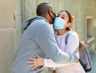 Young woman and man in protective medical masks kissing each other in friendly manner while meeting...