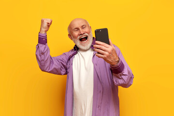 old bald grandfather in purple shirt uses smartphone and celebrates victory with his mouth open