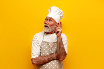 I have an idea. old bald grandfather chef in hat and apron points his finger up on yellow isolated...