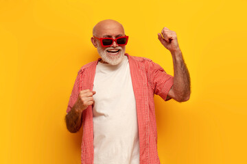 pensioner old grandfather in sunglasses dances and sings to music at party on yellow isolated...