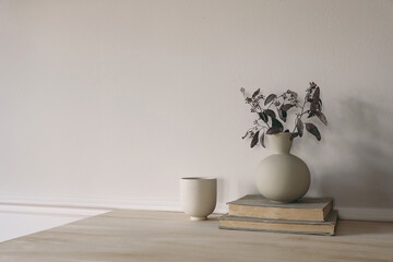 Modern vase with dry eucalyptus tree branches on wooden table. Cup of coffee, pile of old books. White wall background. Scandinavian interior. Elegant home decor. Empty copy space.