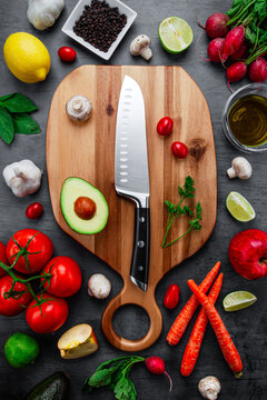 Overhead dark tabletop image of real colorful healthy nutritious raw vegetable and fruit plant-based vegetarian and vegan diet foods placed on a wood cutting board with a clean kitchen knife.
