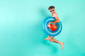 young cheerful guy winner with inflatable swimming ring jumps and flies on blue isolated background...