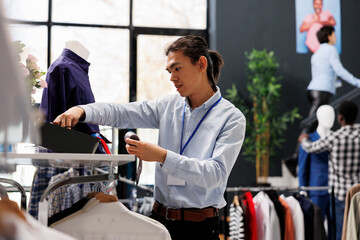 Asian man checking formal belt on store shelf, arranging stylish accessories in clothing store....