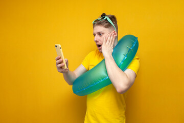 young shocked guy with an inflatable swim ring on vacation in the summer uses a smartphone on a...