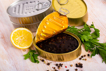Canned seafood. Chopped squid in ink served in open tin can with herbs and lemon on wooden table