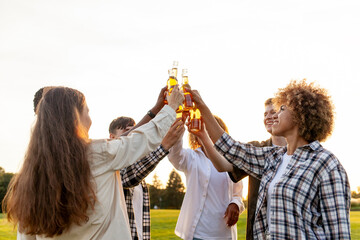 group of multiracial friends at party clinking beer bottles outdoors, interracial women and men...