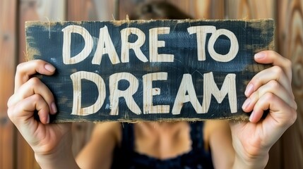 Woman holds sign saying  dare to dream  on blurred background for motivation and success. - obrazy, fototapety, plakaty