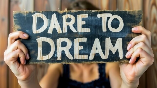 Woman holds sign saying  dare to dream  on blurred background for motivation and success.