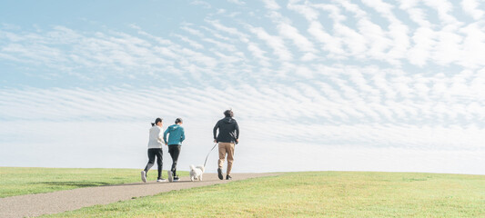 青空の見える公園で犬の散歩・運動・トレーニング・有酸素運動をするさわやかな家族・親子
