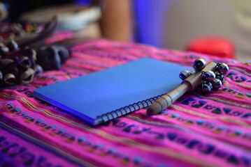 Notas Musicales. Libreta azul, junto a una sonaja de cascabeles sobre prenda rosa tipica mexicana.