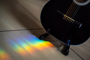 Música. Rayo de luz multicolor cayendo al suelo, guiando hacia el cuerpo de GüitarraAcutica negra con las cuerdas visibles.