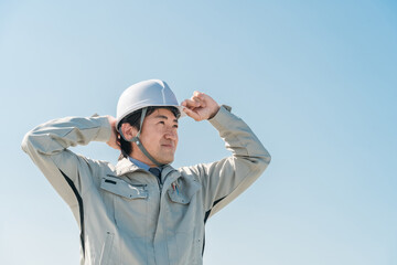 青空の中に立つ作業服を着た作業員（建設・建築・設計・不動産・土木・工事・現場監督・運送）
