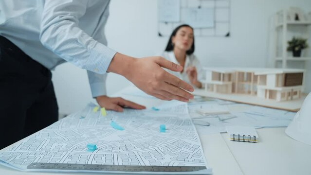 Skilled caucasian interior designer working with house model while discussing with asian architect engineer about house plan on meeting table with blueprint and house model scatter around. Immaculate.