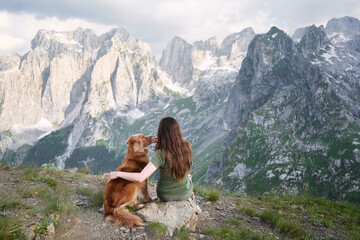 Naklejka na ściany i meble Companionable moment with pet in the mountains. A woman and her loyal dog sit together, gazing at the grand alpine scenery surrounding them
