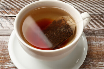 Tea bag in cup with hot drink on wooden rustic table, closeup