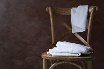 White terry towels on wooden chair against brown background. Space for text