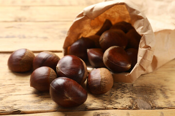 Sweet fresh edible chestnuts in paper bag on wooden table, closeup