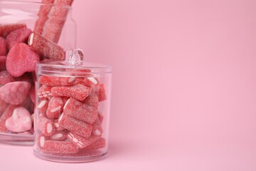 Tasty candies in glass jars on pink background, closeup. Space for text