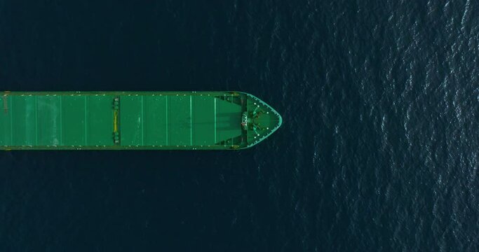 Top-down view of green bulk carrier anchored at sea on calm water during the day