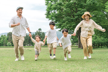 芝生の公園で手を繋いで走る家族・ファミリー（レジャー・アウトドア・ピクニック・キャンプ）
