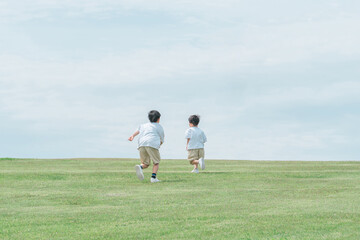 芝生の丘で追いかけっこする活発な子供達・兄弟・走る
