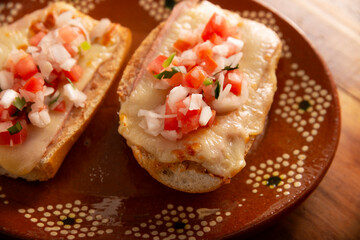 Molletes. Mexican recipe based on bolillo bread split lengthwise, spread with refried beans and gratin cheese, adding pico de gallo sauce and some protein such as ham, bacon or chorizo.