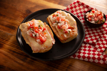 Molletes. Mexican recipe based on bolillo bread split lengthwise, spread with refried beans and gratin cheese, adding pico de gallo sauce and some protein such as ham, bacon or chorizo.