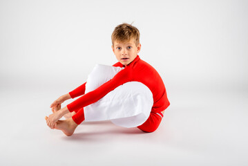 Barefoot little boy in red pajamas sitting up with a surprised expression while holding his pillow 