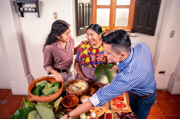 A young Latino couple collaborates in the preparation of corn tamales, led by an older woman of the...