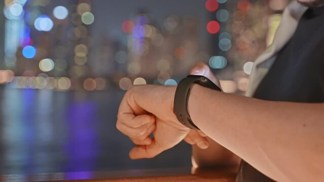 Man citizen using smartwatch touching screen at night on waterfront in city.