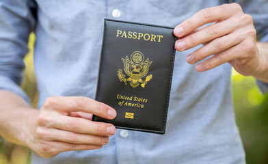 Close-up view of a mans hands holding presenting an United States passport, travel legality readiness or traveling to the USA, North America, immigration and emigration abstract concept, one person
