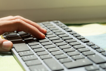 A persons hand is laying on the keys of a sleek modern design business office keyboard, suggesting writing blogging freelance work or everyday computer use concept, natural daylight, closeup shot