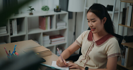 Selective focus, Side view,Female writer sitting at desk writing notes while working on tablet for...