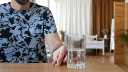 A man taking a pill from the table with a glass of water