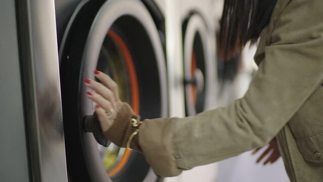 A contemporary woman with crimson nails begins her laundry routine by shutting the washing machine door.