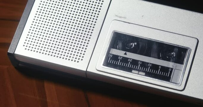 Close-up view of a vintage cassette player lying on a wooden table top, with a cassette playing.