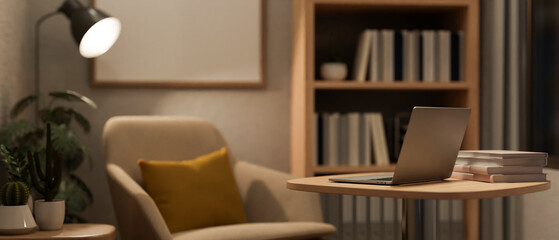 A modern home office at night with a laptop on a table, an armchair, and dim light from a floor lamp