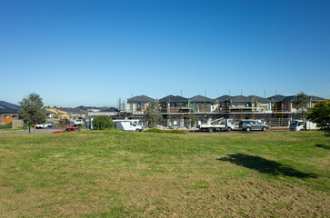 A vacant lot of land with grass lawn with some new townhouses under construction in the background. Concept of development in a new residential neighbourhood, suburban homes and Australia real estate. © Doublelee