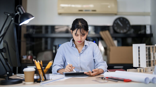 Asian architect engineer women working to checking about drawing architecture plan on digital tablet while creative to designing new project about building model and construction architectural plan
