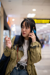 Fototapeta premium A young Asian female traveler is talking on the phone with someone while walking in the airport.