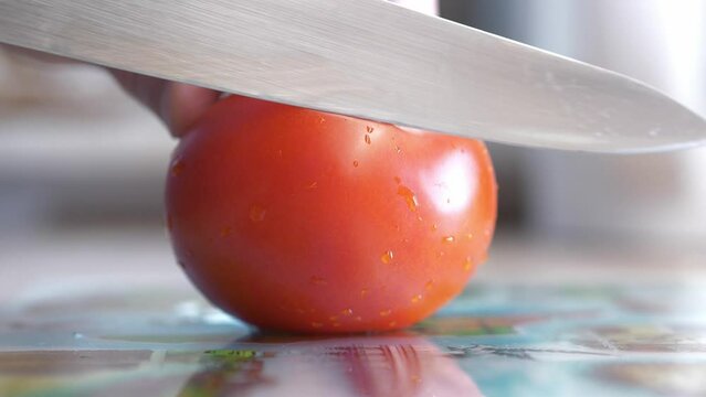 sharp chef's knife slicing tomato on cutting board close up in slow motion
