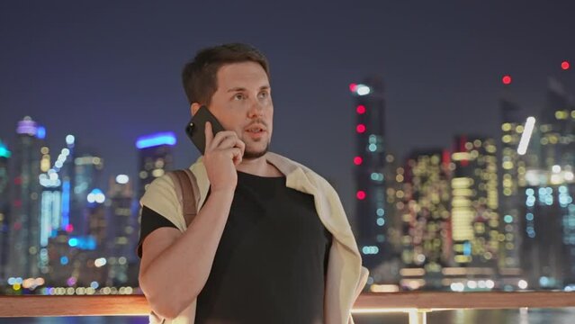 Man talking on smartphone in megapolis downtown at night on waterfront.