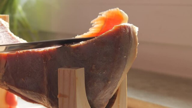 Spanish traditional pork jamon. A knife cuts a piece of hamon meat into thin slices in the kitchen